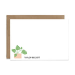 An image of a flat note and a kraft brown envelope. The card has an illustrated monstera potted plant and an example of a name in the bottom left corner.
