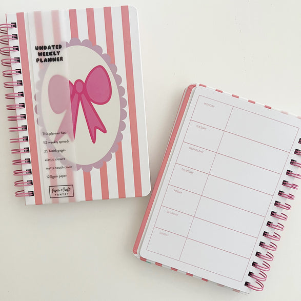 Two spiral-bound planners with pink and white design on a light background