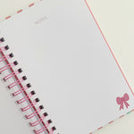 Notebook with pink ribbon and decorative bow on a white background