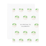 A folded greeting card with text that reads "So matcha to celebrate!" with cute illustrated matcha cups. Card is lying on a white envelope.