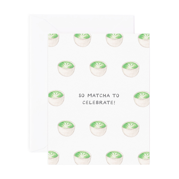 A folded greeting card with text that reads "So matcha to celebrate!" with cute illustrated matcha cups. Card is lying on a white envelope.