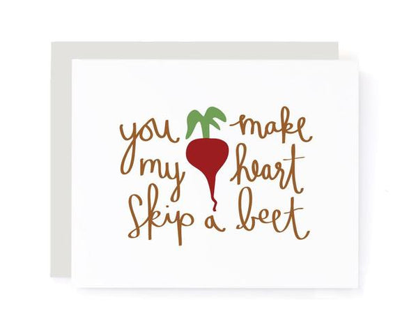 A folded greeting card with text that reads "you make my heart skip a beet" with an illustrated beet. Card is lying on a light grey envelope.