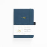 An image of deep blue dot grid bullet journal with a gold foil stork scissors on the cover. The journal is laying on a white background.