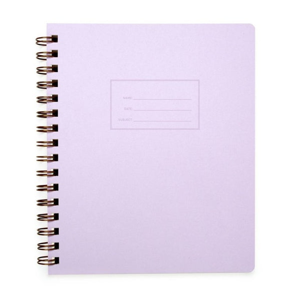 An image of a lilac purple notebook with gold spiral binding on a white background. The cover of the notebook has a small section to label the name, date and subject.