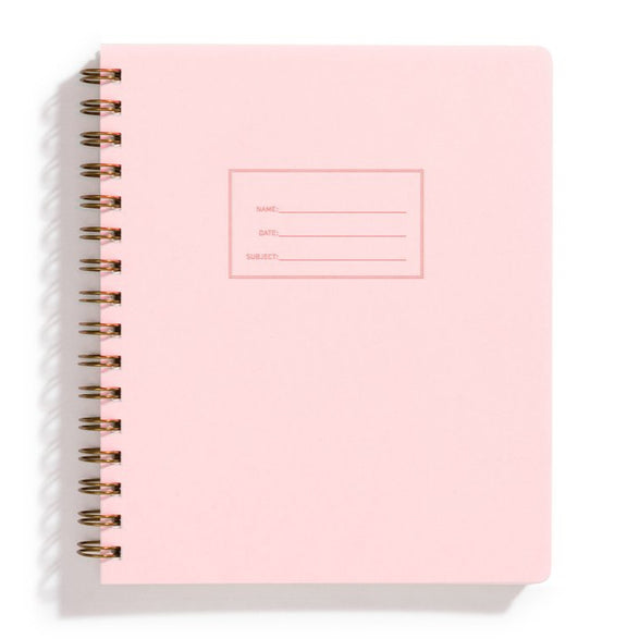 An image of a light pink notebook with gold spiral binding on a white background. The cover of the notebook has a small section to label the name, date and subject.