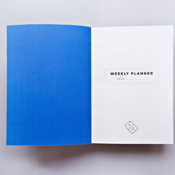 An image of an open weekly planner with a royal blue inside cover and text "Weekly Planner Year:___" on the front page.