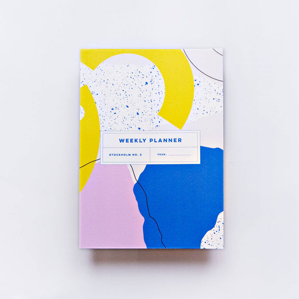 An image of a weekly planner with an abstract yellow, pink, blue and white design. There is text "Weekly planner Stockholm No. 2 Year:___" on the middle of the front cover.