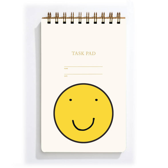 An image of a white Shorthand task pad with spiral binding and a giant yellow smiley face on the cover